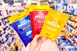 hand holding three bags of halls cough drops