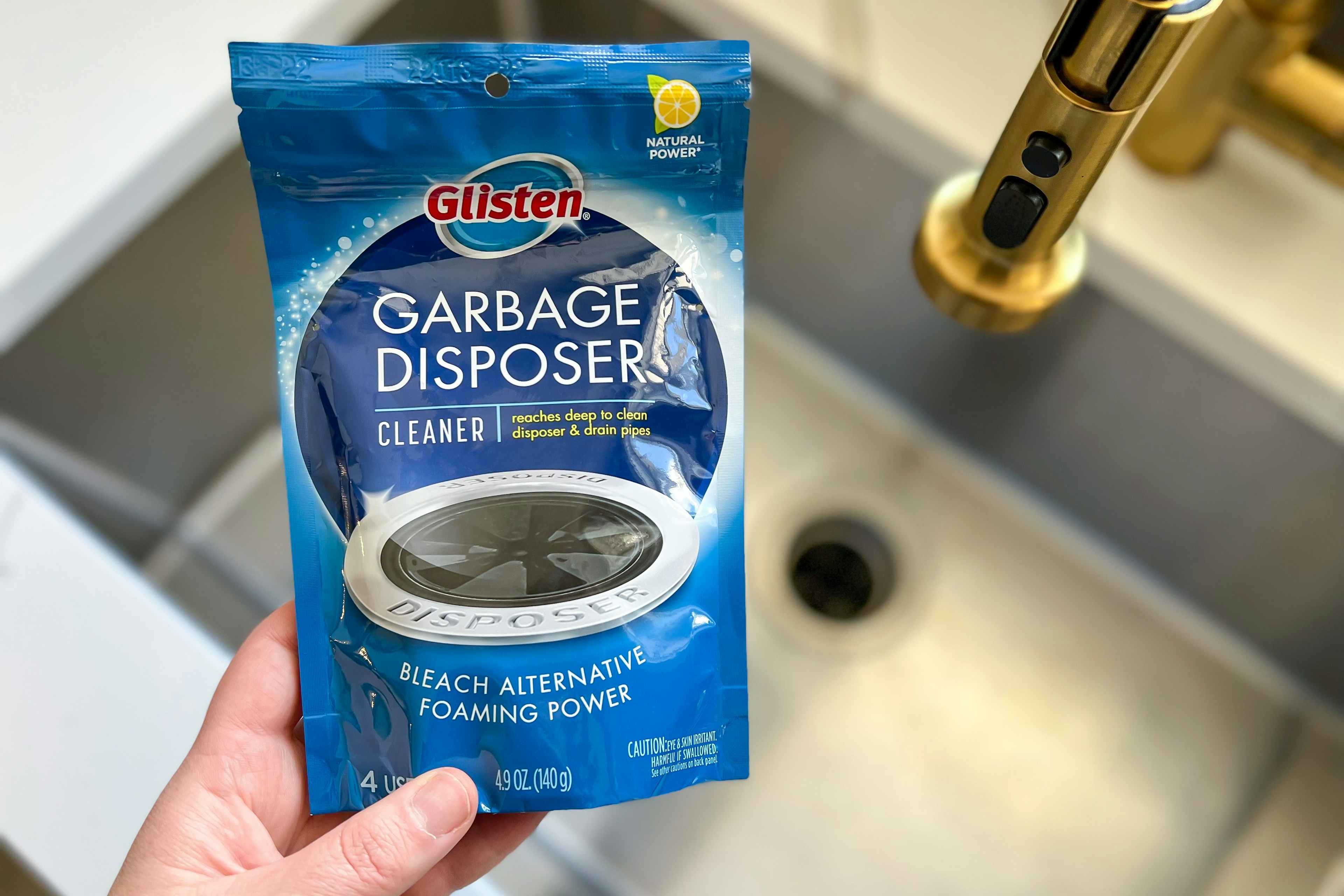 someone holding glisten garbage disposer cleaner next to sink