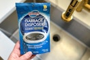 someone holding glisten garbage disposer cleaner next to sink