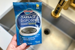 someone holding glisten garbage disposer cleaner next to sink