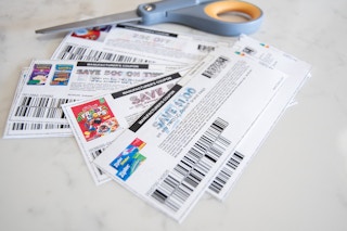 A pile of printed coupons laying on a counter next to a pair of scissors.