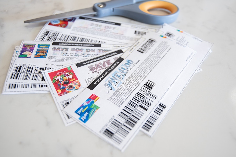 A pile of printed coupons laying on a counter next to a pair of scissors.