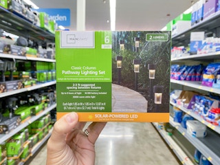 Hand hold a box of six Mainstays Solar Lights in outdoor lighting aisle at Walmart.
