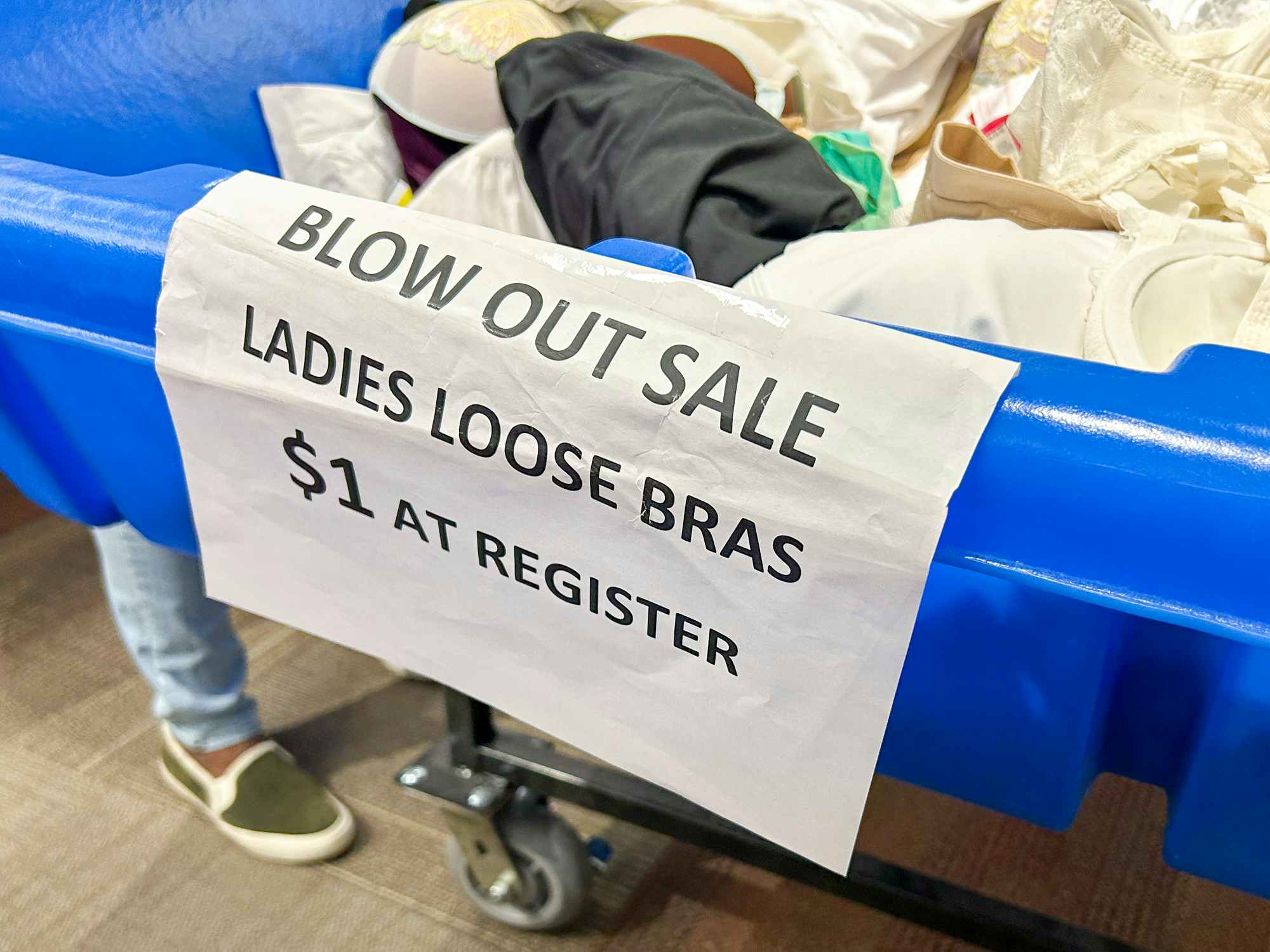 A bin with bras in it with a sign that says "Blow out sale. Loose bras $1 at register"