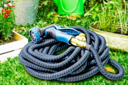 Lifestyle image of the blue Kotto Expandable Garden Hose outdoors in the grass