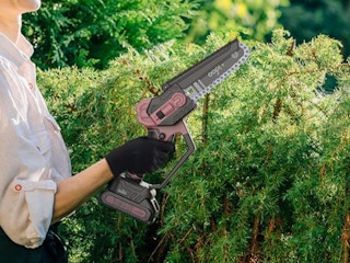 person holding chainsaw in front of bushes