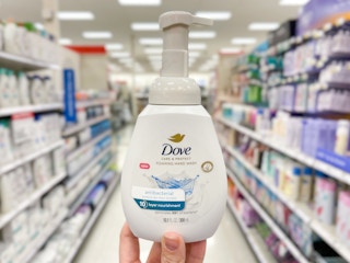 A Dove hand soap held out in front of a store aisle by hand.