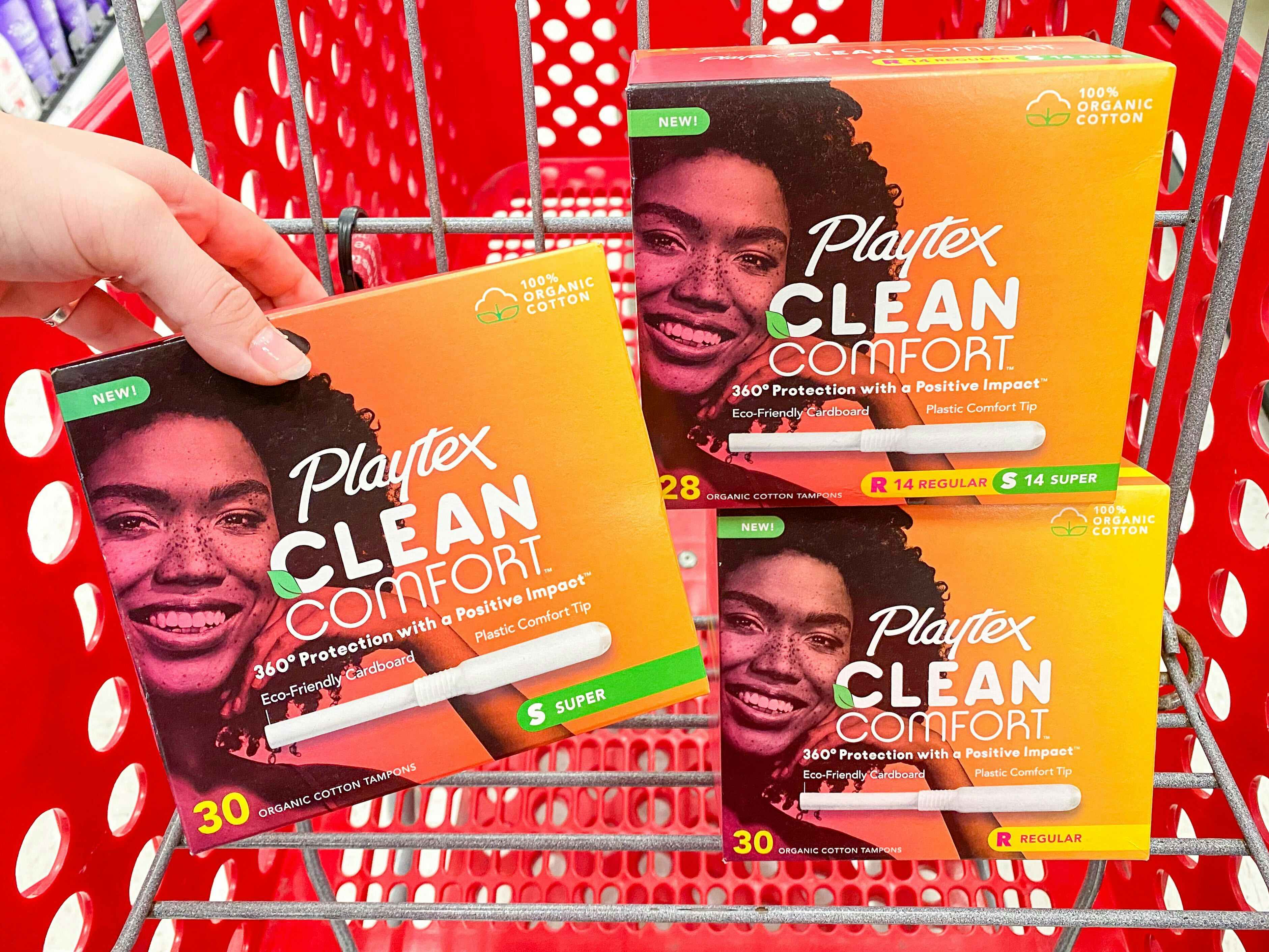 Hand holding up 1 box of Playtex tampons in front of a Target shopping cart that has two other boxes of Playtex tampons in it