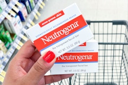 hand holding two boxes of Neutrogena facial bars in front of shopping cart