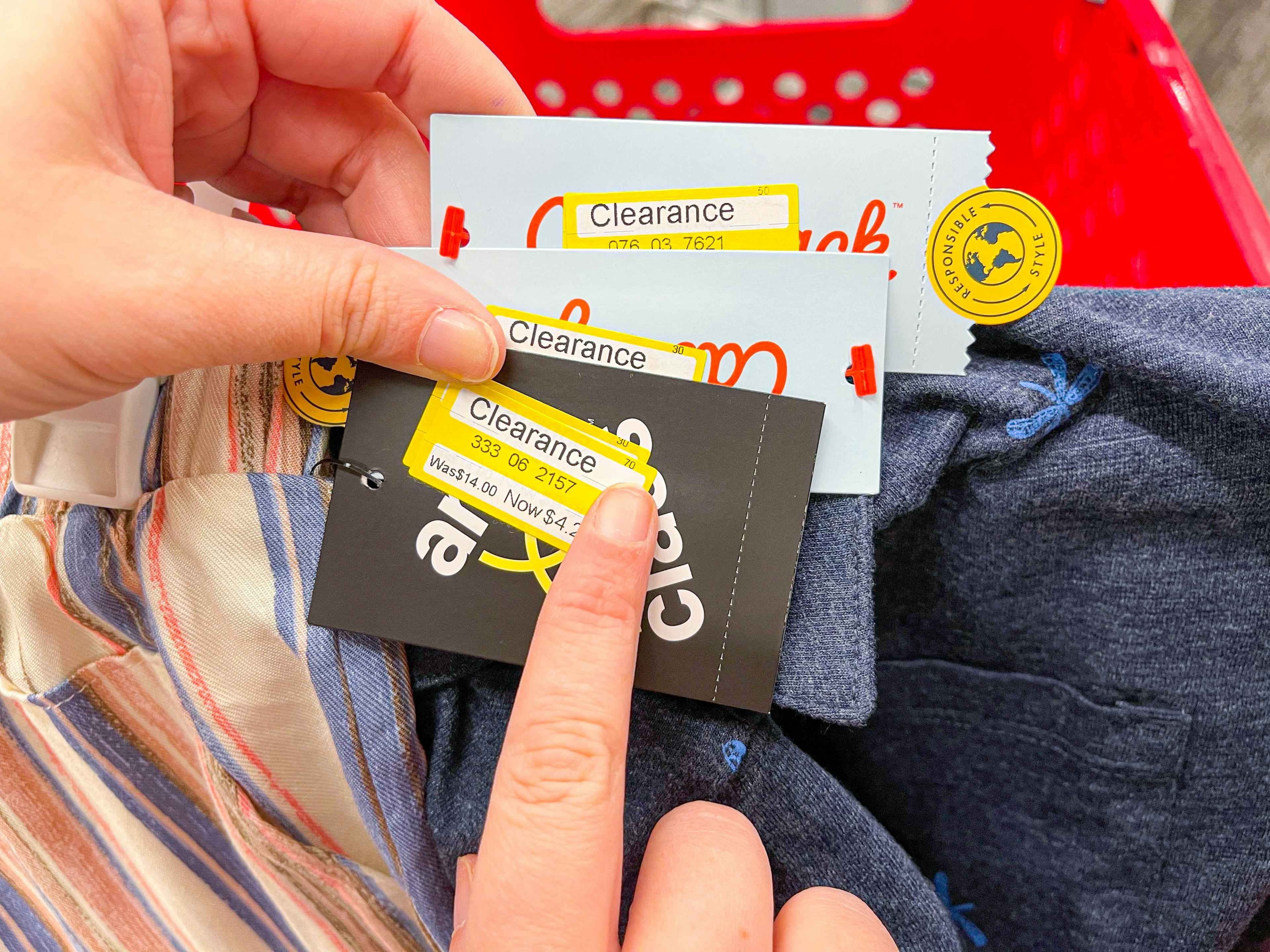 A person's hands holding some Target clearance clothing and pointing to the clearance sticker on one of the tags.