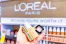 person holding loreal foundation, eyeshadow, and lipstick in front of the loreal display