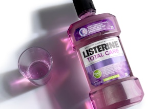 A bottle of Listerine Total Care Anticavity Mouthwash lays on its side next to a small glass of Listerine.