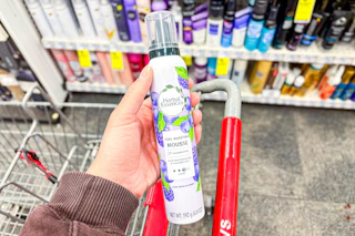 person holding herbal essences mousse over a cart