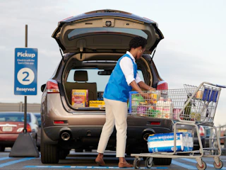 A Sam's Club employee packing groceries into the trunk of a vehicle that is parked in the Curbside pickup parking spot outside of Sam's ...