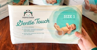 A person holding a pack of Amazon Mama Bear diapers, with other packages in the background.