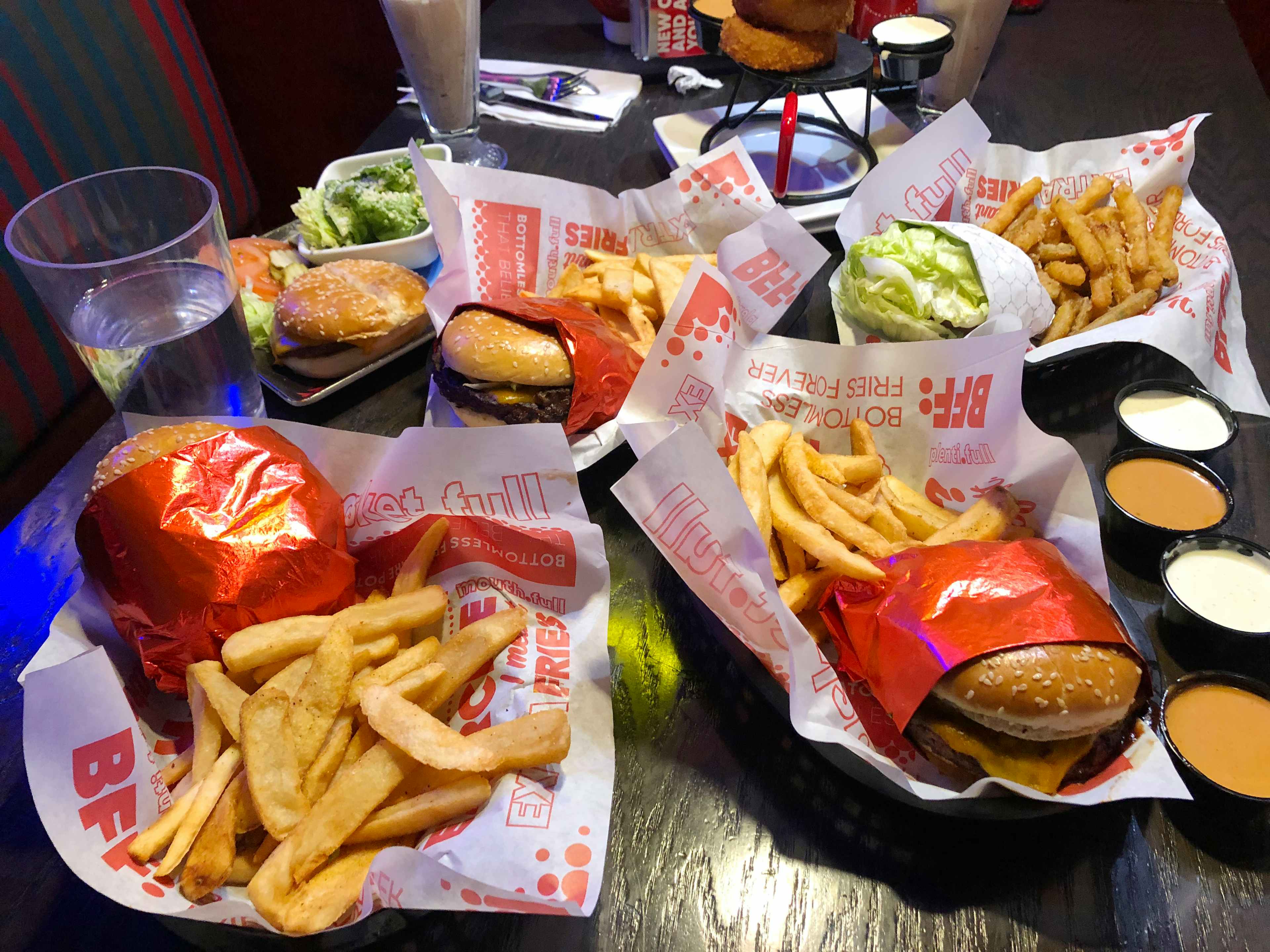 A table at Red Robin with multiple plates of food, including burgers, fries, broccoli, a tower of onion rings, a milkshake, and several ...
