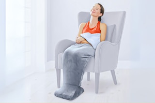 Lifestyle image of woman sitting in a chair wearing a Sharper Image Massaging Blanket