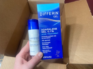 hand holding differin adapalene retinoid acne gel over an amazon box