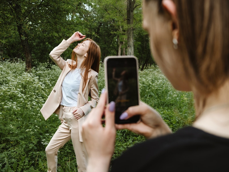 A person taking a photo of another person posing in front of some greenery