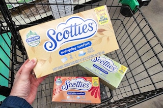 person holding a box of scotties facial tissues over a cart with more boxes in it