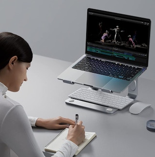 A woman writing in front of a laptop sitting on a stand