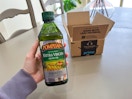a hand holding a bottle of olive oil in front of an Amazon box