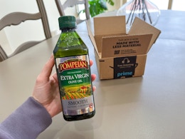 a hand holding a bottle of olive oil in front of an Amazon box