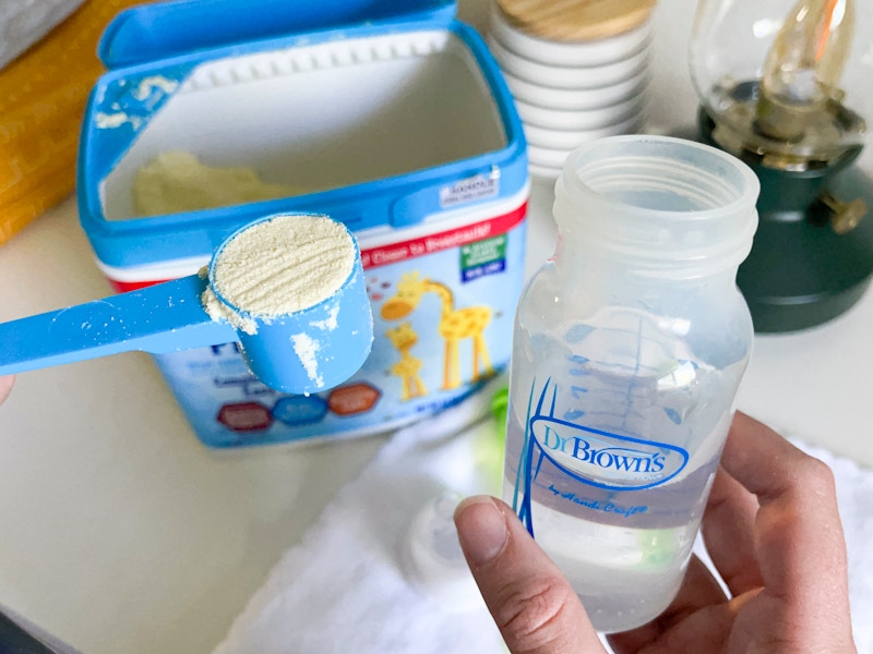 A person putting a scoop of Kirkland powdered baby formula into a bottle.