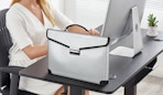 a person sitting at a desk with a silver fireproof document bag and a computer on the desk