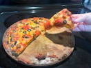 a person grabbing a pizza off a pizza stone