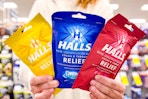 person holding three bags of halls cough drops