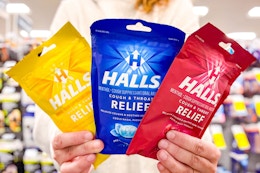 person holding three bags of halls cough drops