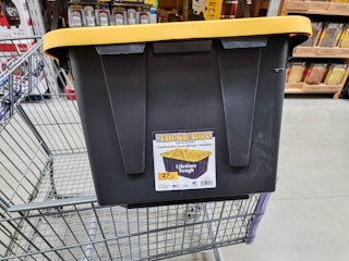 a black 27 gallon storage tote with a yellow lid in a cart