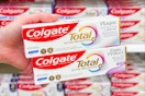 hand holding 2 colgate total toothpaste in front of a target shelf