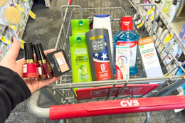 person holding revlon nail polish and maybelline eyeshadow over a cart with garnier, dove, colgate, and therabreath products in it