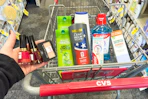person holding revlon nail polish and maybelline eyeshadow over a cart with garnier, dove, colgate, and therabreath products in it