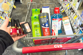 person holding revlon nail polish and maybelline eyeshadow over a cart with garnier, dove, colgate, and therabreath products in it
