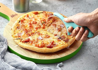 A person cutting a pizza on a pizza peel.