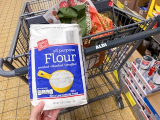 A person holding a bag of flour next to an aldi shopping cart.