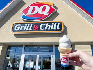 Someone holding a Dairy Queen soft serve cone in front of a Dairy Queen storefront.