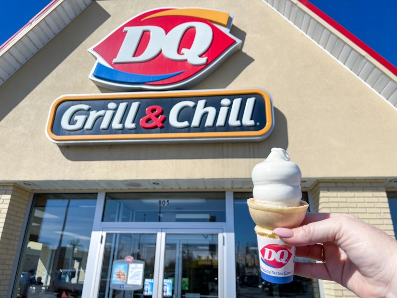 Someone holding a Dairy Queen soft serve cone in front of a Dairy Queen storefront.