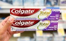 hand holding two boxes of Colgate Total toothpaste in the aisle