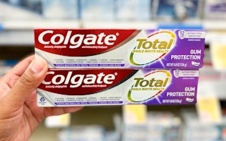 hand holding two boxes of Colgate Total toothpaste in the aisle