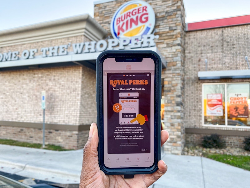 Burger King app with roayl perks page open, held in front of a Burger King restaurant.