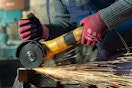 Two hands wearing red safety gloves made of spandex and nitrile uses a power tool that gives off sparks.