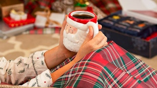 A person sitting by a Christmas tree, holding a vintage Santa mug