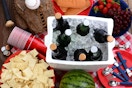 Cooler with a bowl of chips, red cups utensils and a watermelon