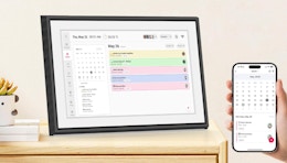 a digital calendar on a wooden nightstand next to someone holding a phone