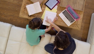 Parent helping child with homework with tablet, book and laptop on a table