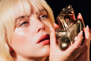 Billie Eilish holding a bronze bust perfume bottle